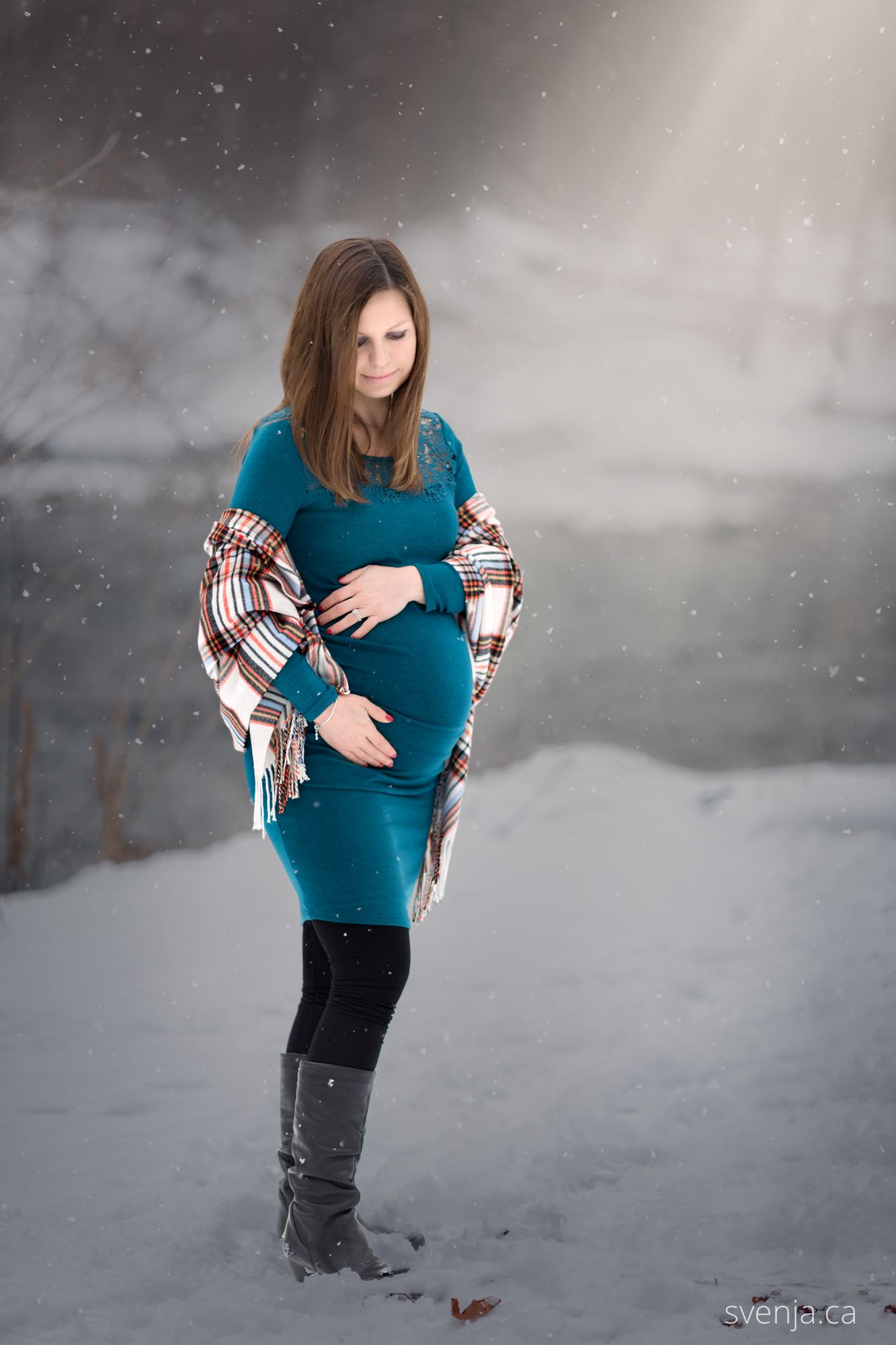 maternity picture with woman outside in the snow with sunlight looking down at her baby