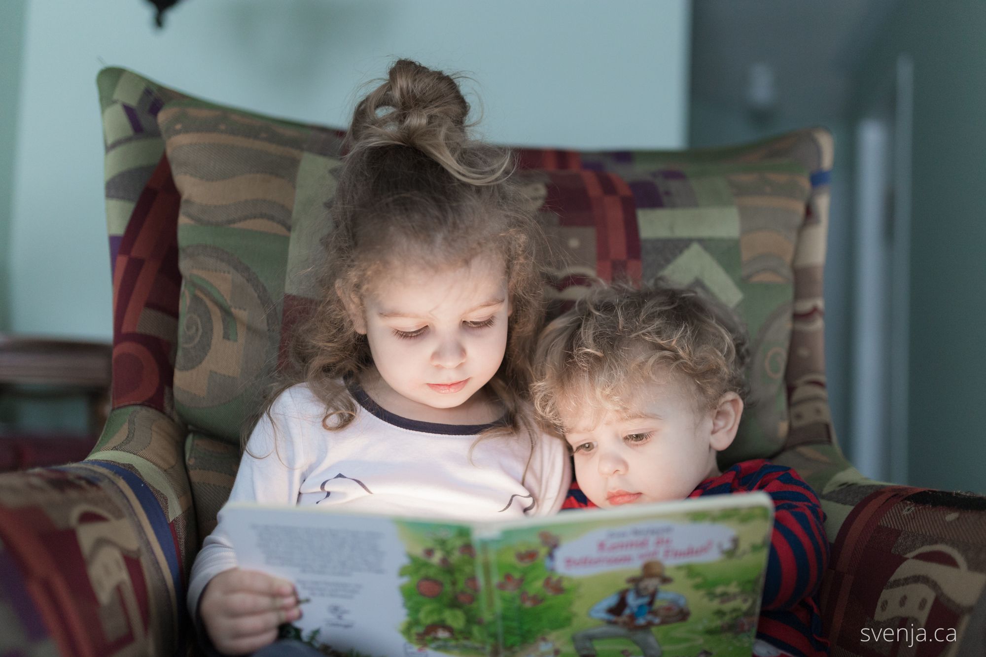 two young children sit on a chair and read a book together