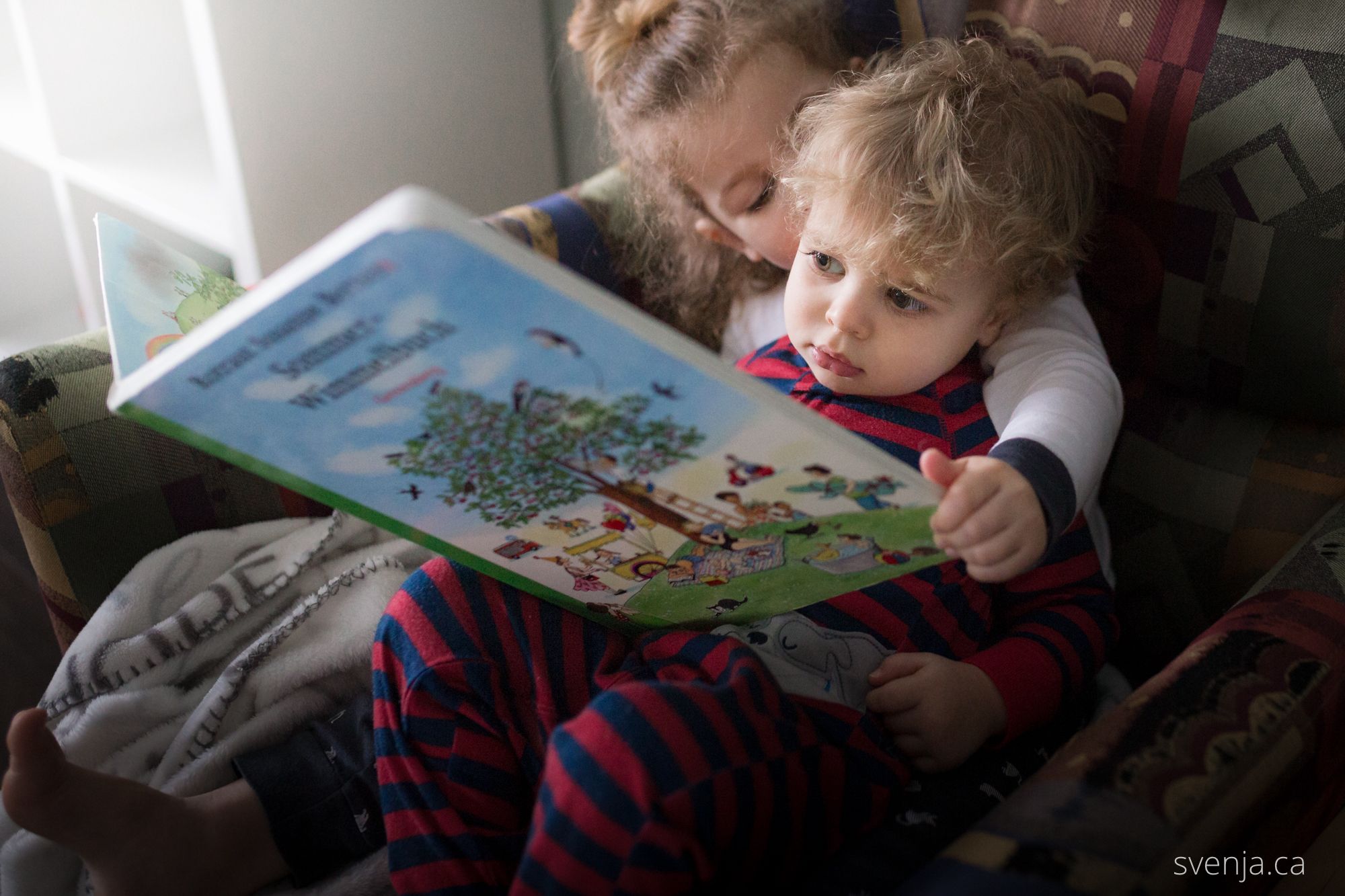 a big sister holds her little brother while reading a book