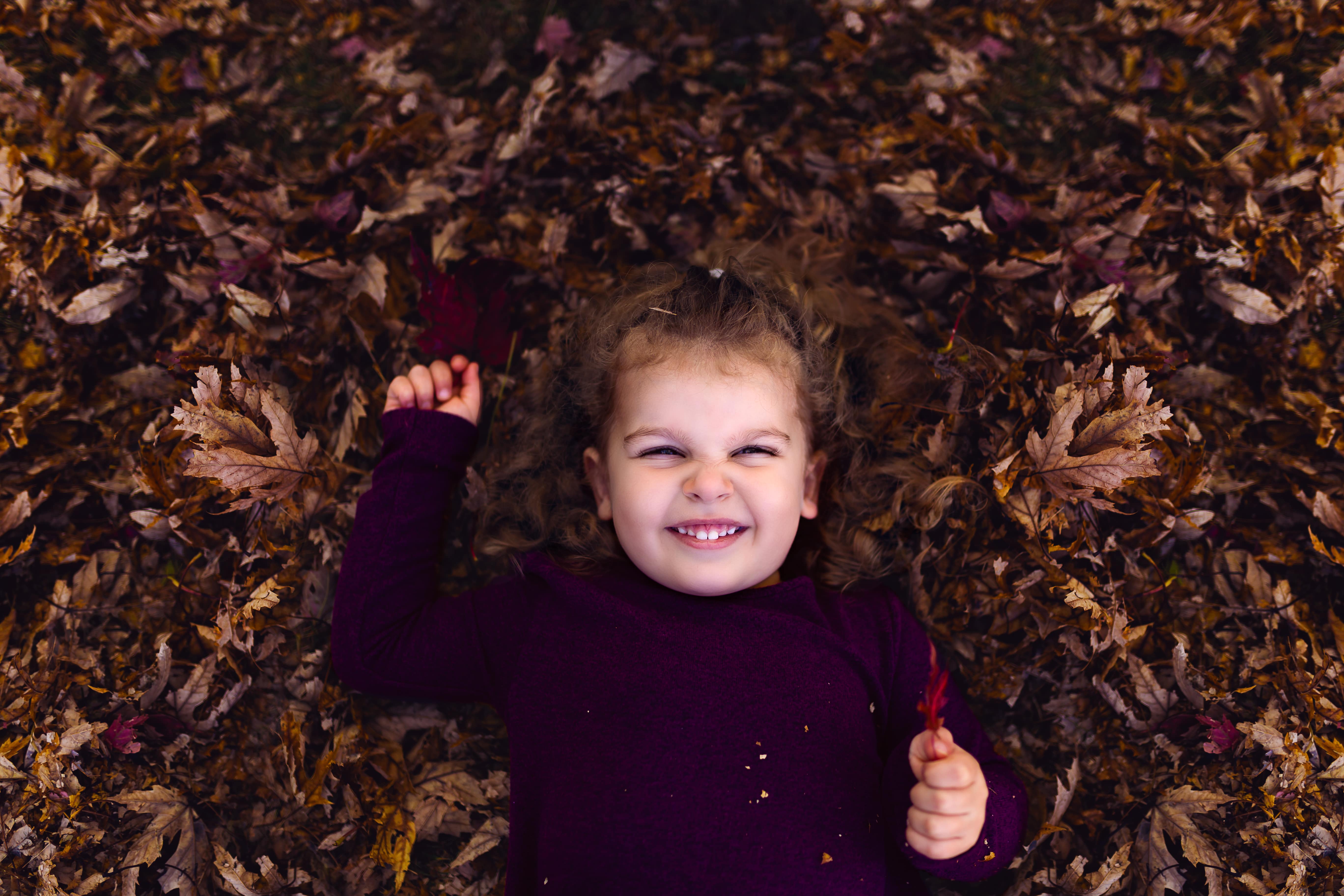 little girl lays in leaves in autumn