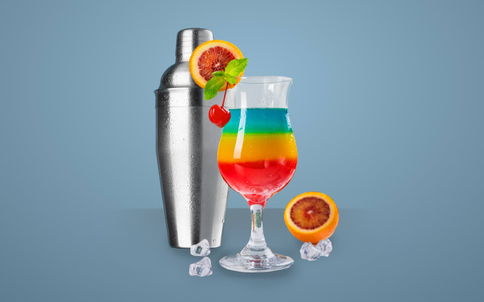 A metal shaker next to a hurricane glass with a striped rainbow cocktail inside for Confetti's Virtual Make Your Own Mixology Kit