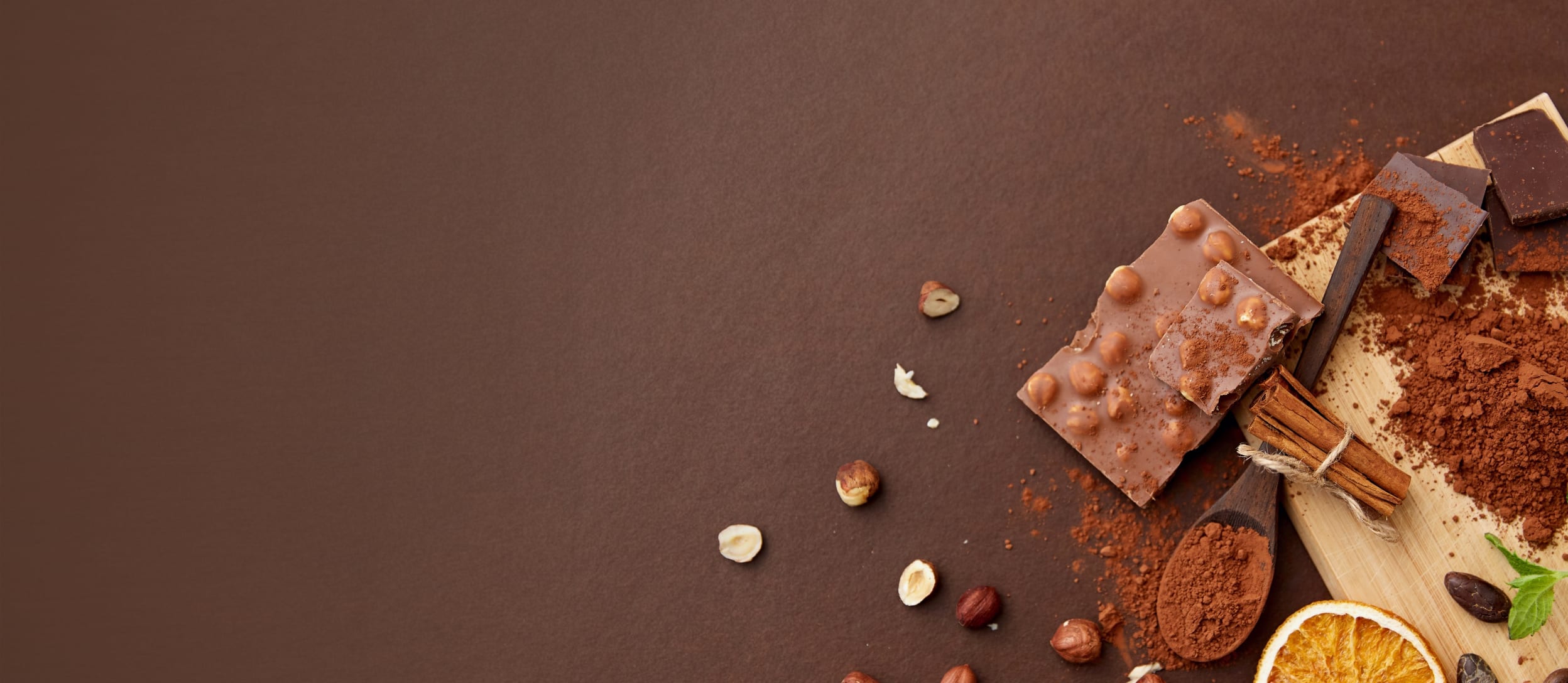 A cutting board with cocoa powder, cinnamon sticks, crushed hazelnuts, and a chocolate bar on it and scattered around for Confetti's Virtual Chocolate Tasting Team Building