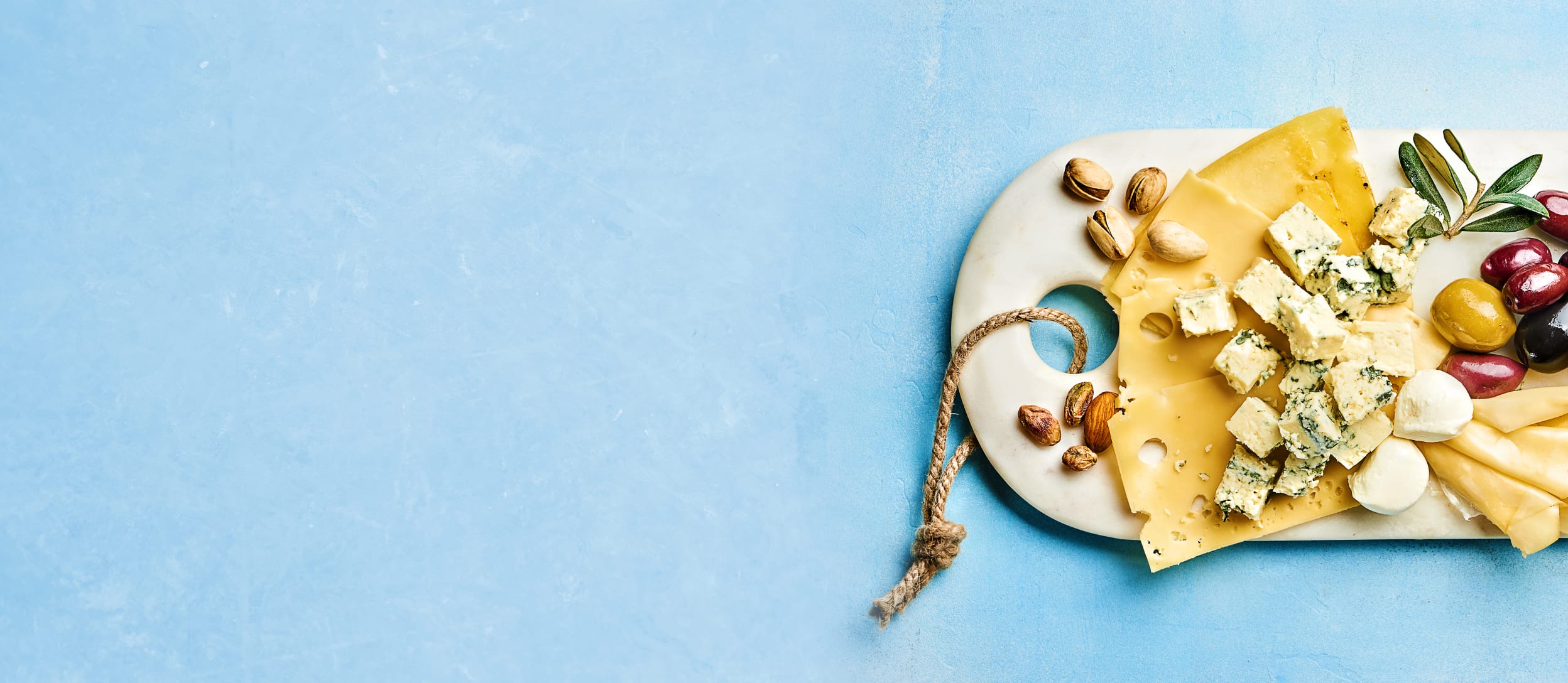 A birds eye view of a white charcuterie board covered in a variety of hard and soft cheeses and fruits for Confetti's Virtual Food Tasting Kits