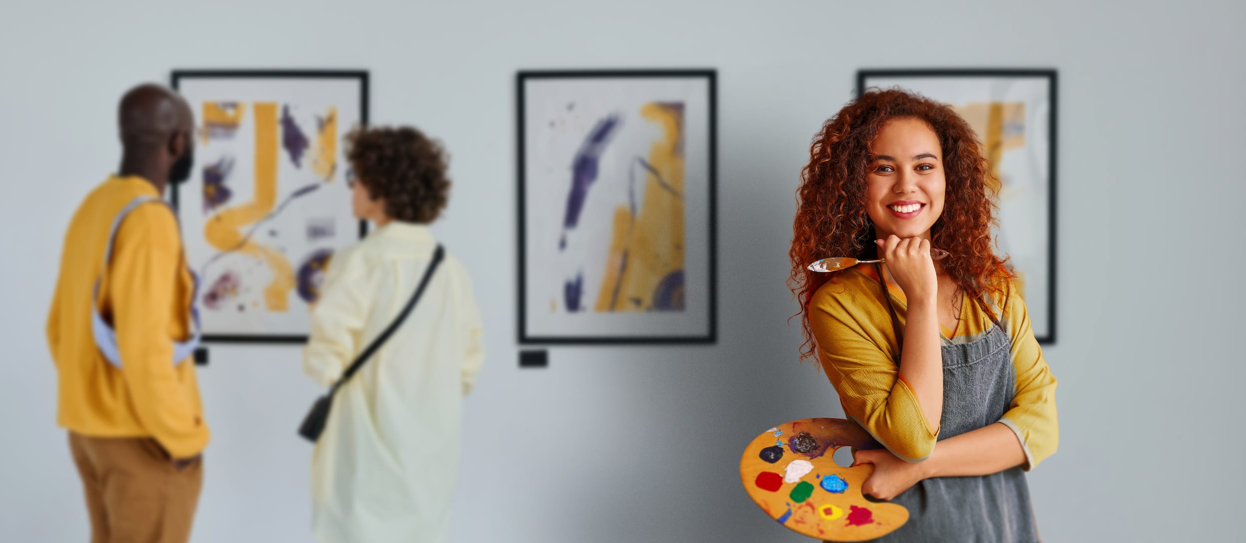 Black woman holding a paintbrush and palette with people in the background looking at modern paintings