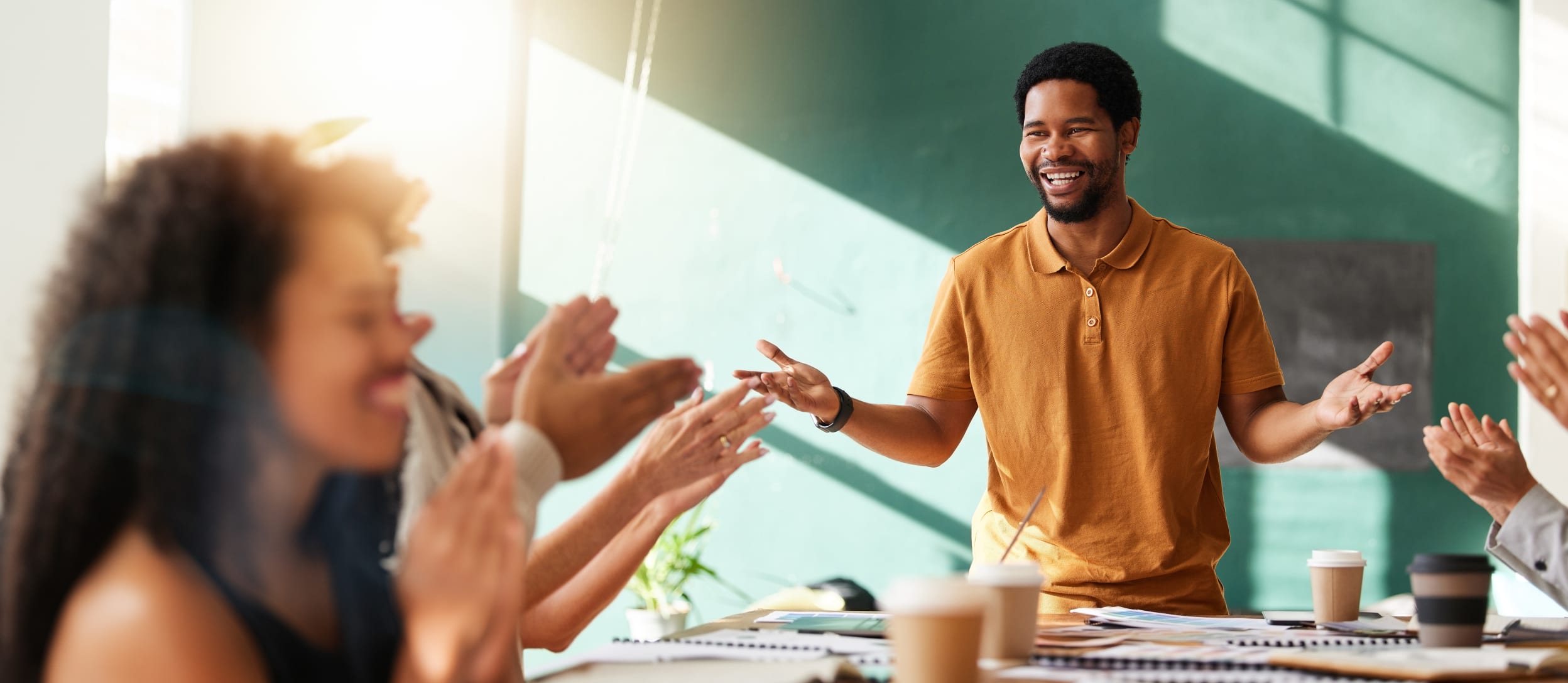 Black man teaching a class in a well-lit classroom with a blackboard and students applauding (large)