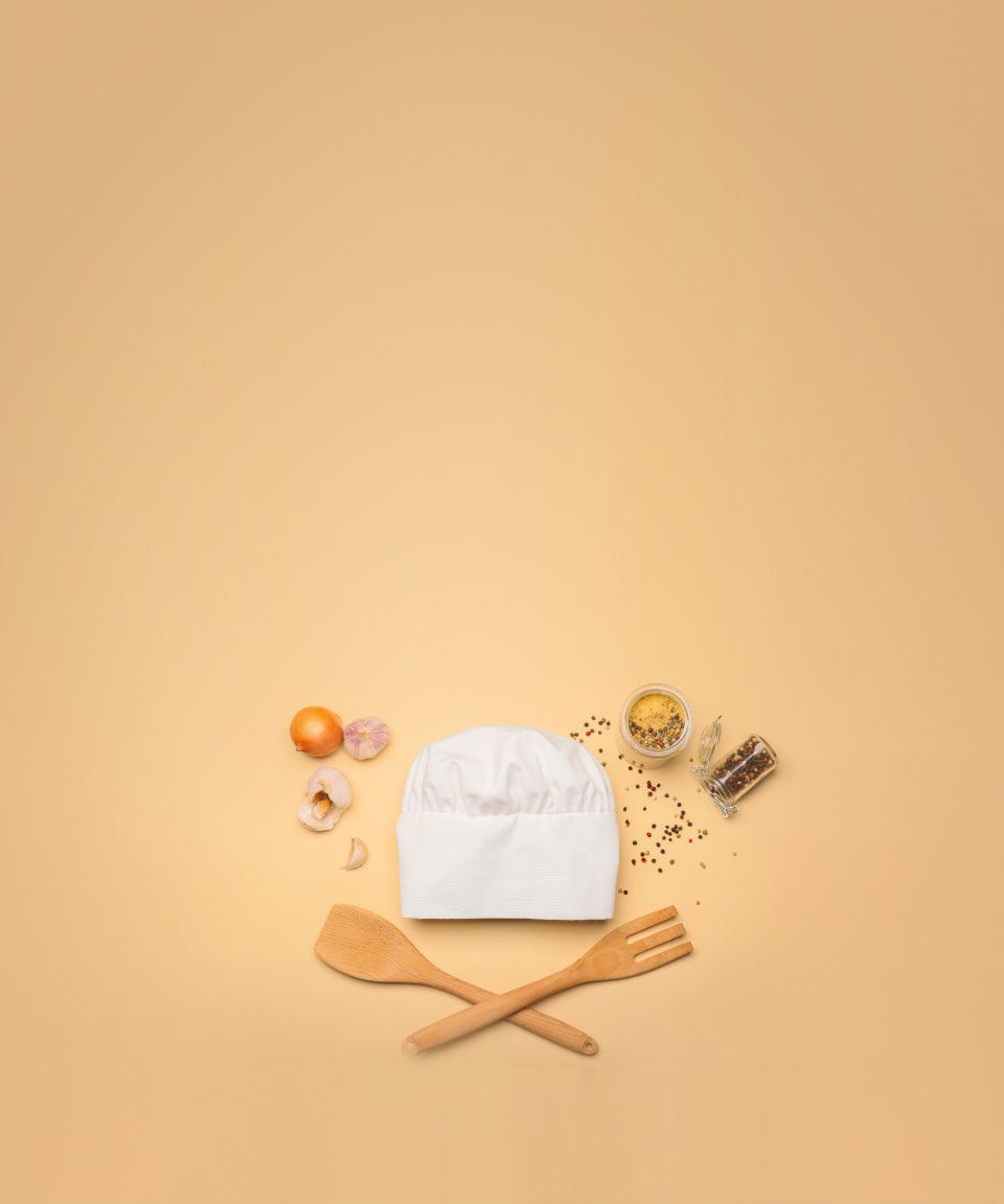 A chefs hat, wooden spatula and fork, onions and garlic, and spilled spices and peppercorns for Confetti's Virtual Cooking Basics Class