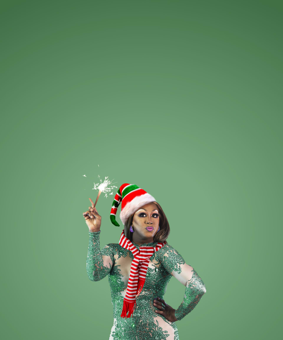 A drag queen wearing an elf hat and scarf, and holding a sparkler for Confetti's Virtual Holiday Drag Queen Trivia