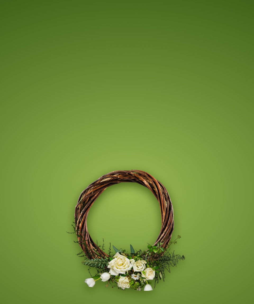 A brown wreath with white spring florals and greenery at the bottom for Confetti's Virtual Spring Wreath Making Class