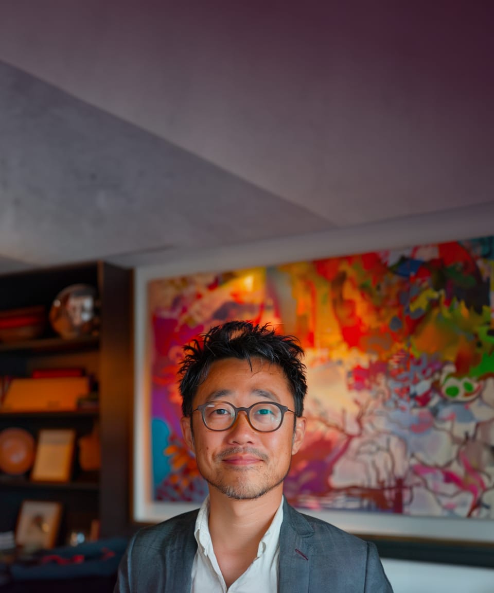 Man dressed in a suit smiling in a home office with a bookshelf and painting (small)