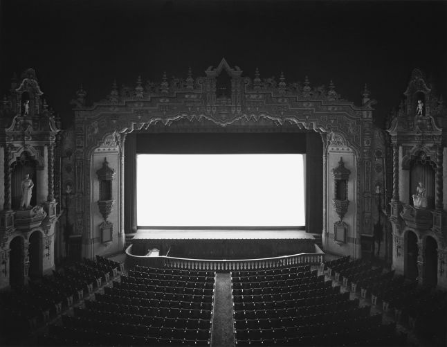 Hiroshi Sugimoto: AKRON CIVIC OHIO (1980). In der Mitte der 70er Jahre begonnenen Serie «Theatres» fotografierte Sugimoto alte amerikanische Kinosäle und Drive-Ins mit einer klappbaren 4x5 Kamera und einem Stativ. Exakt zu Beginn der Vorführung drückte Sugimoto auf den Auslöser. Die Belichtungszeit dauerte exakt so lange, wie der Film, der gezeigt wurde. Durch die lange Belichtungszeit ist auf den Fotos von den Filmen nichts zu erkennen – die Leinwand ist nichts als eine weisse Fläche –, während die architektonischen Details und Sitze hervortreten.
