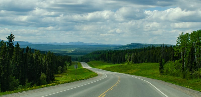 the alaska highway going through rolling hills and green forests with road visibile far in the distance