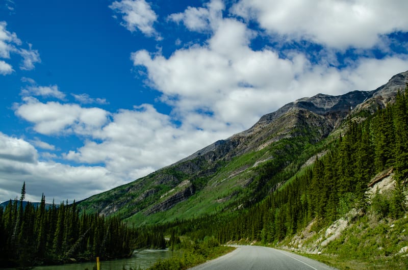 road following a river along the base of a mountain