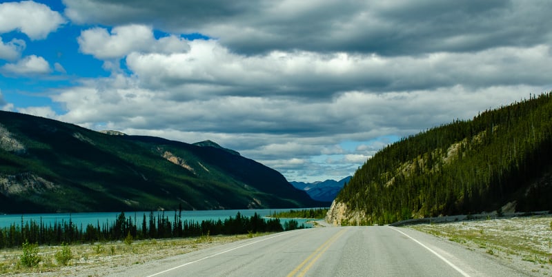 road descending to muncho lake with steep cliffs along the road