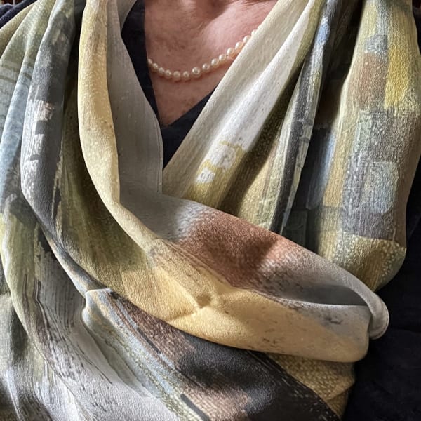 This pastel landscape scarf is 17 inches wide and 64 inches long in 100% silk crepe de chine. The rolled hem is beautifully stitched with well-formed corners. The design is from my 2019 abstract painting “Yellow Mirage”, and the color is sumptuous with gold and peach, muted green and grey. I wear one of my scarves every day, even in the house. They drape beautifully and feel wonderful around the neck.