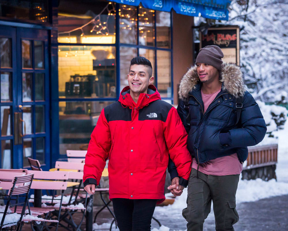 Two people holding hands and walking through snowy Whistler Village