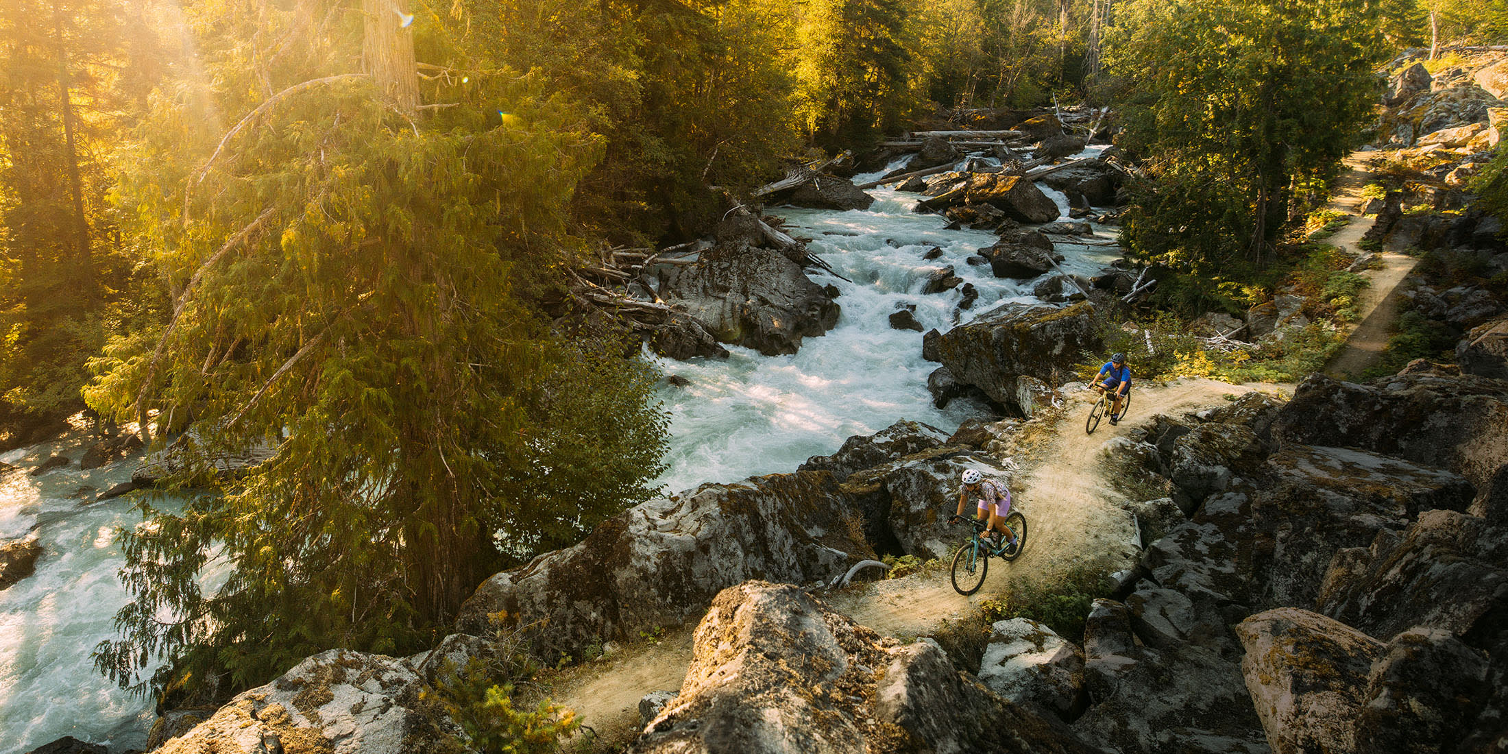 Two people gravel biking Gord's Garden on the Sea to Sky Trail beside the Cheakamus River in Whistler, British Columbia.