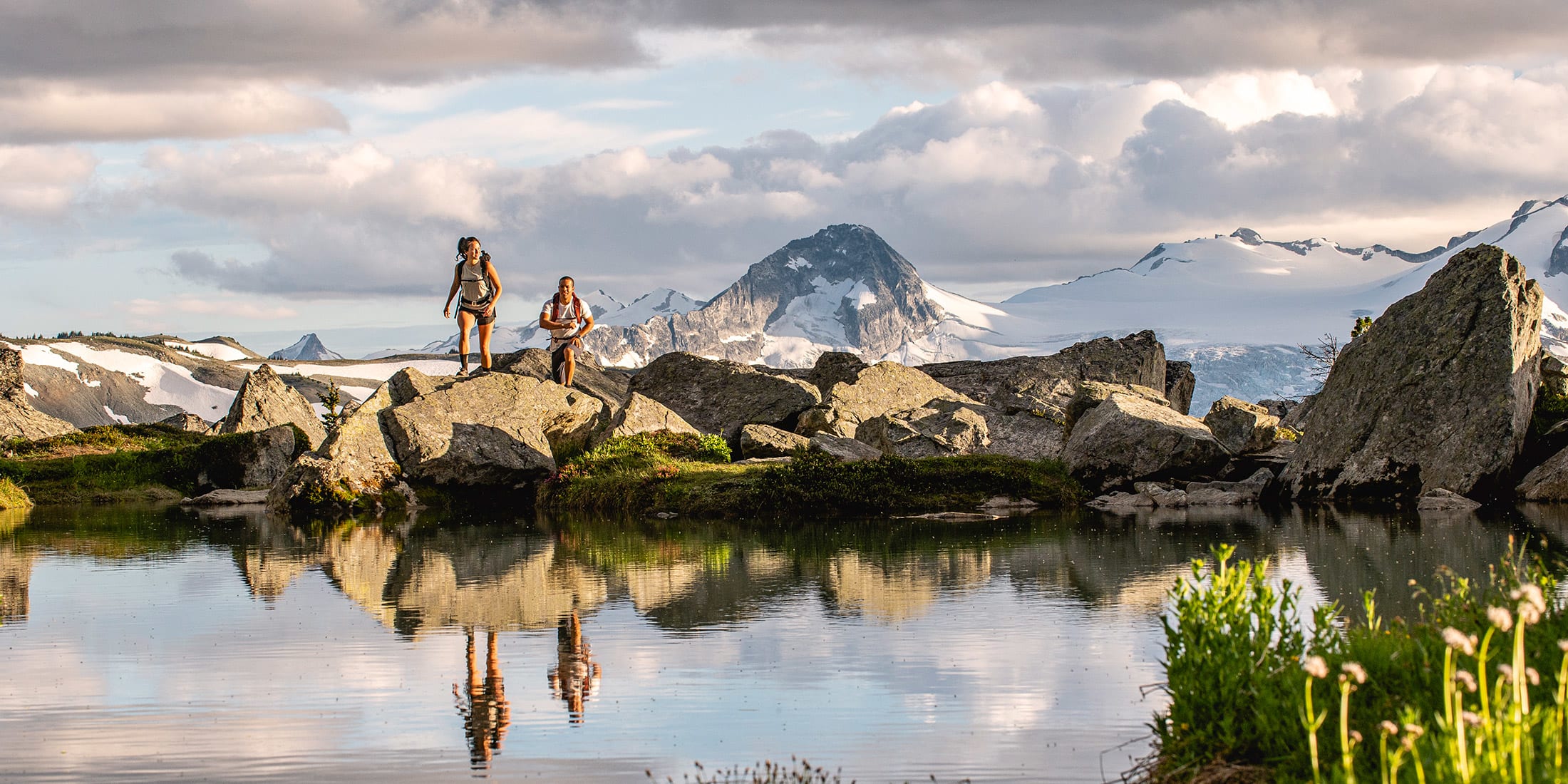 Two people walking across large boulders beside a high alpine lake in Whistler British Columbia