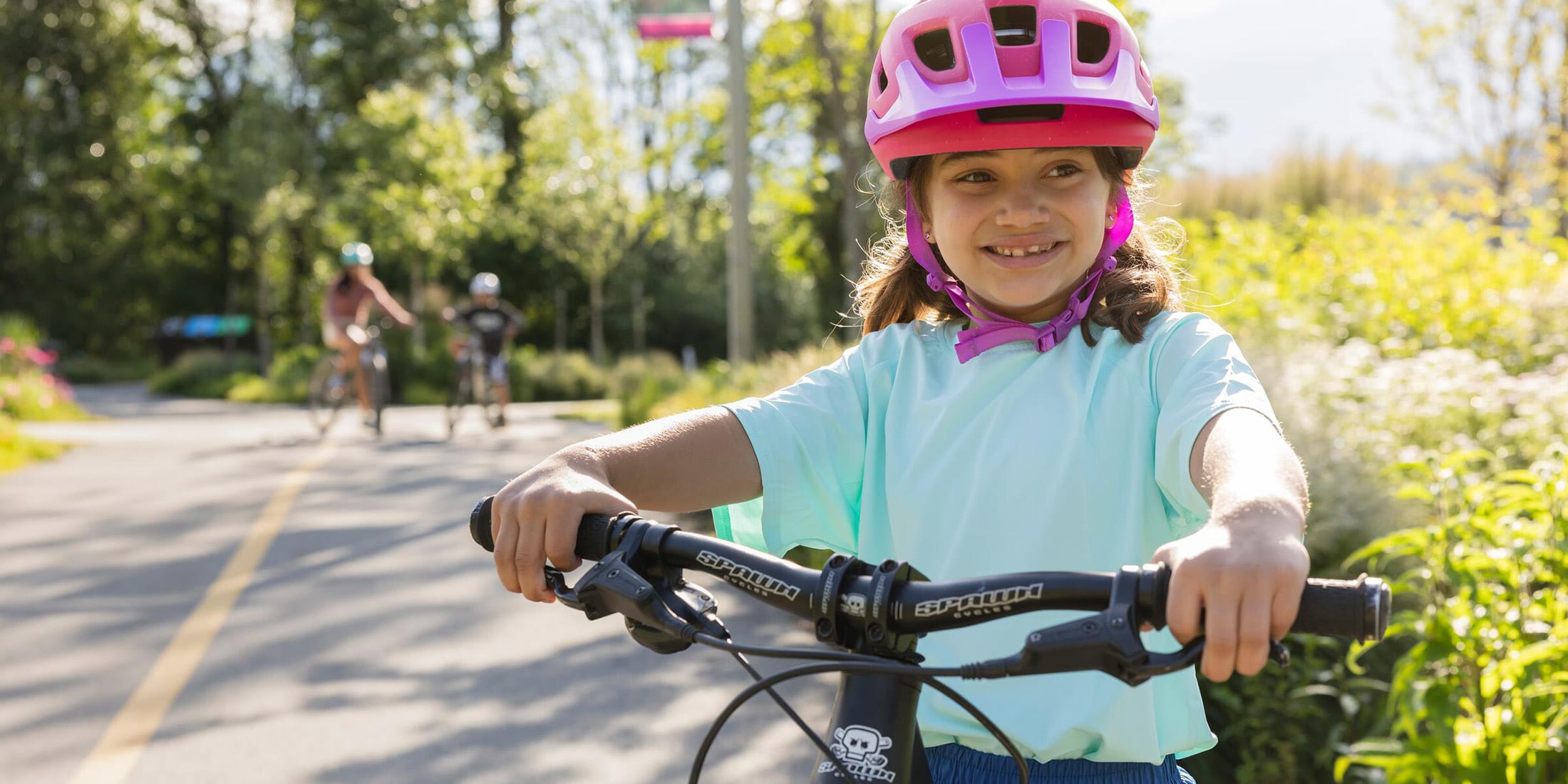 A young child smiling while straddling their bike on the Valley Trail at Rainbow Park on Alta Lake