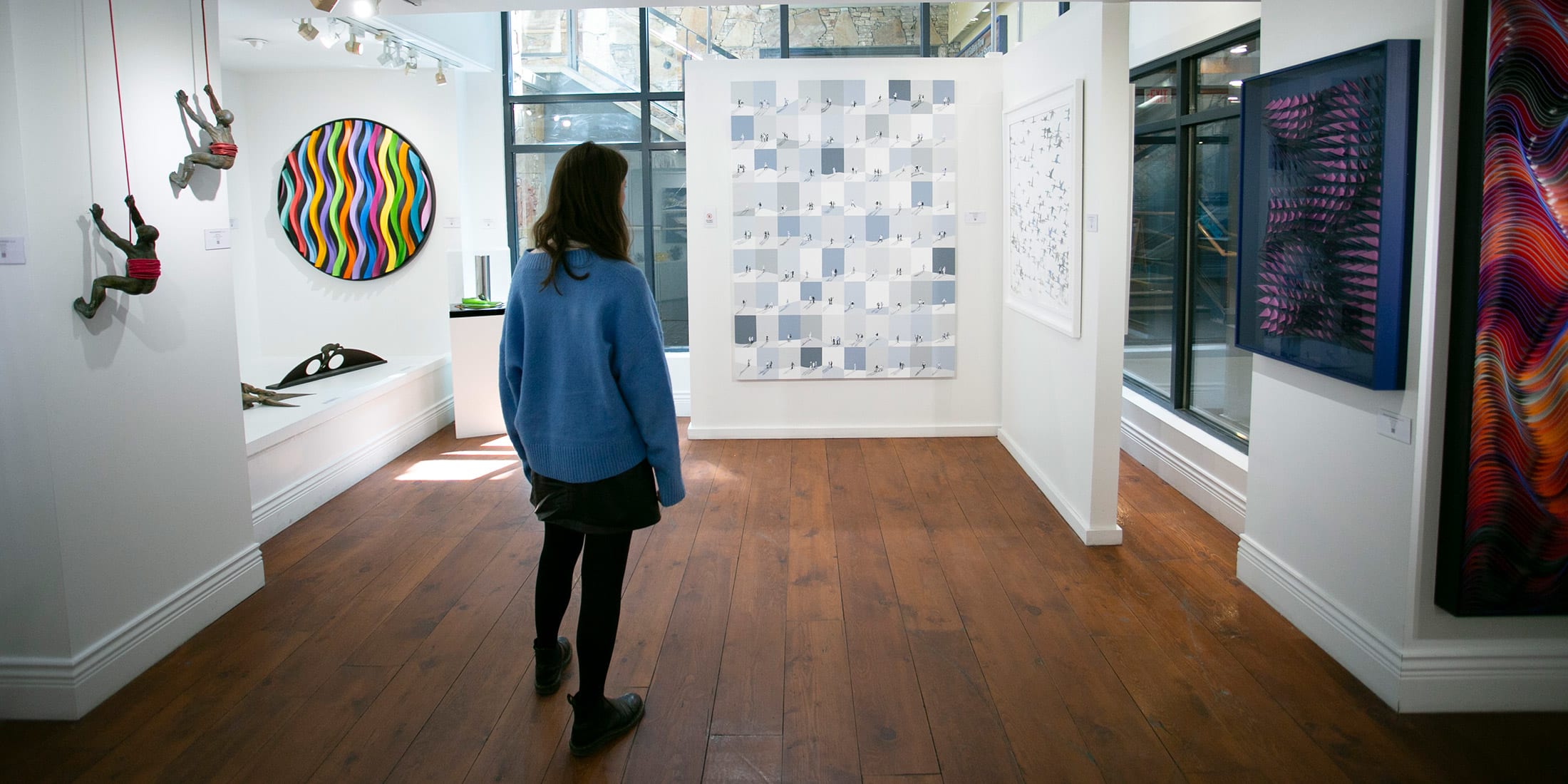 A woman in a blue sweater explores the Whistler Contemporary Art Gallery, surrounded by bold, colourful and thought-provoking pieces. Natural light filters in through large windows, blending mountain-town charm with creative expression.