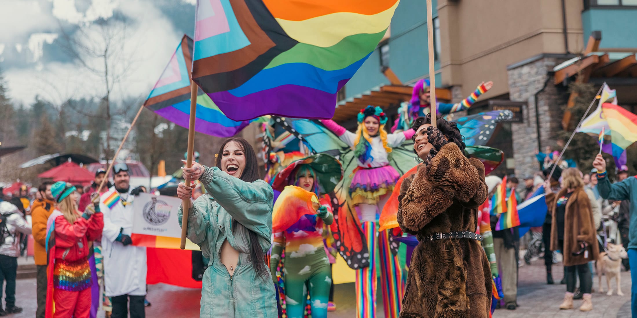 A crowd of people with flags and costumes celebrating Whistler Pride Festival in Mountain Square