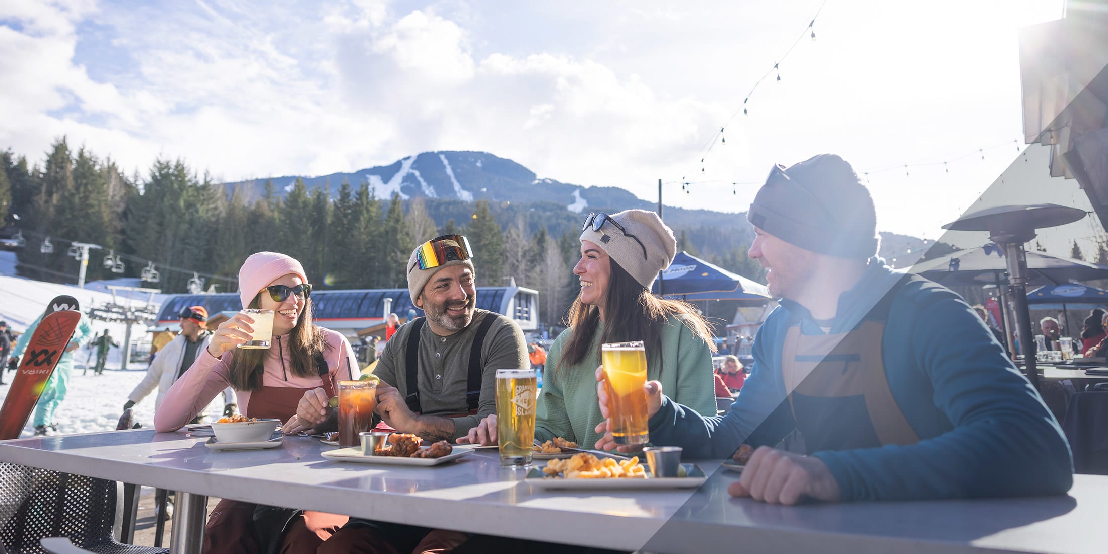 A small group of people wearing ski gear and sitting at a table enjoying apres-ski at the base of Blackcomb Mountain