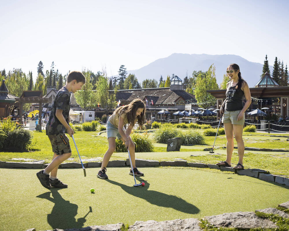 Family playing mini golf at the Family Adventure Zone on a sunny day in Whistler