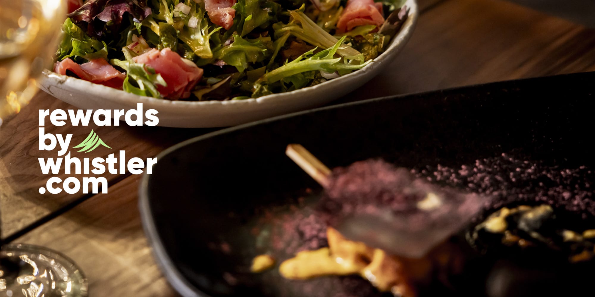 Rewards by Whistler.com logo over a close-up of a restaurant meal with fresh salad and shared dishes, highlighting dining experiences in Whistler.