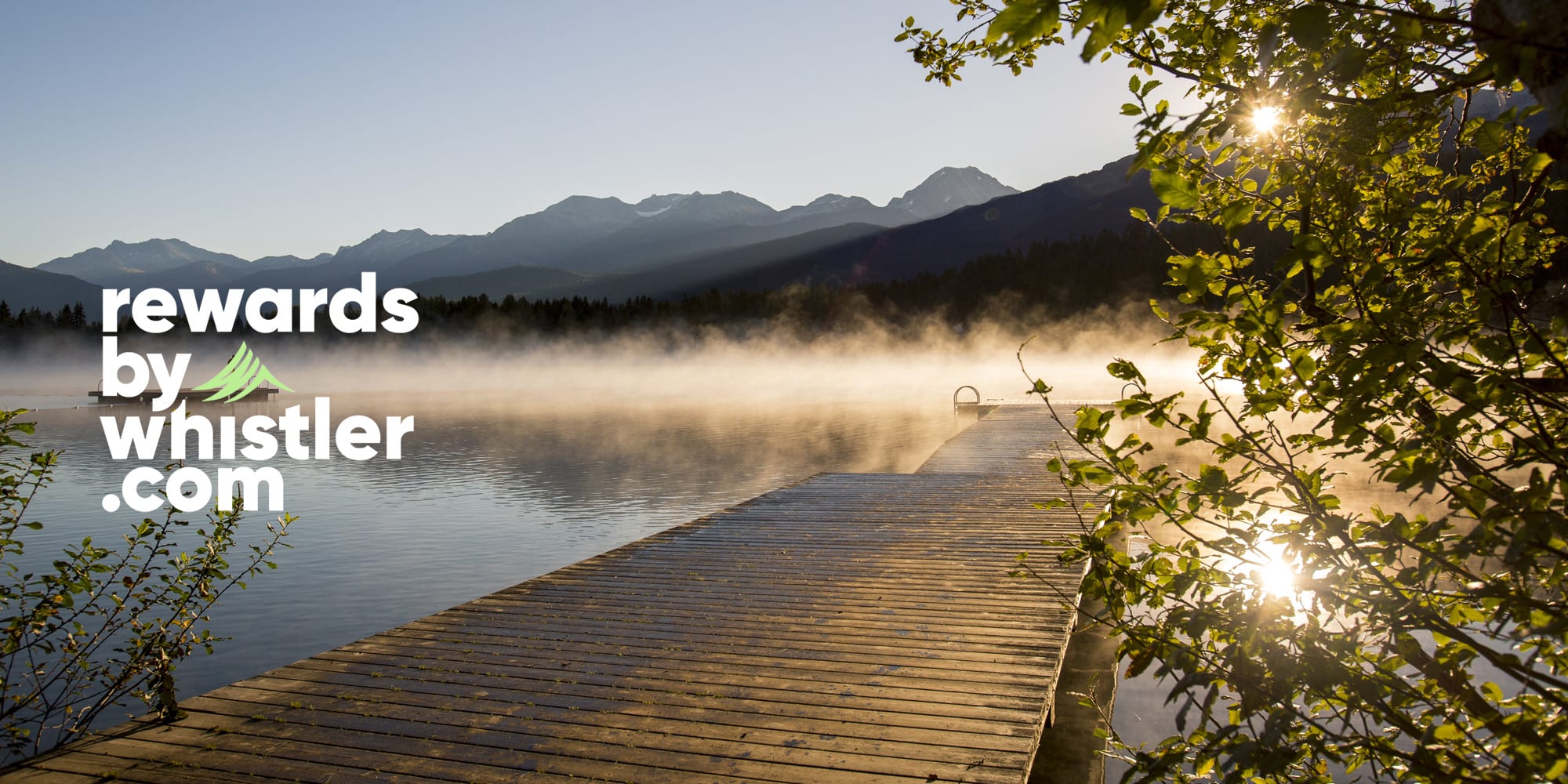 Sunrise over a misty lake in Whistler, with a wooden dock, mountain views and the Rewards by Whistler.com logo.