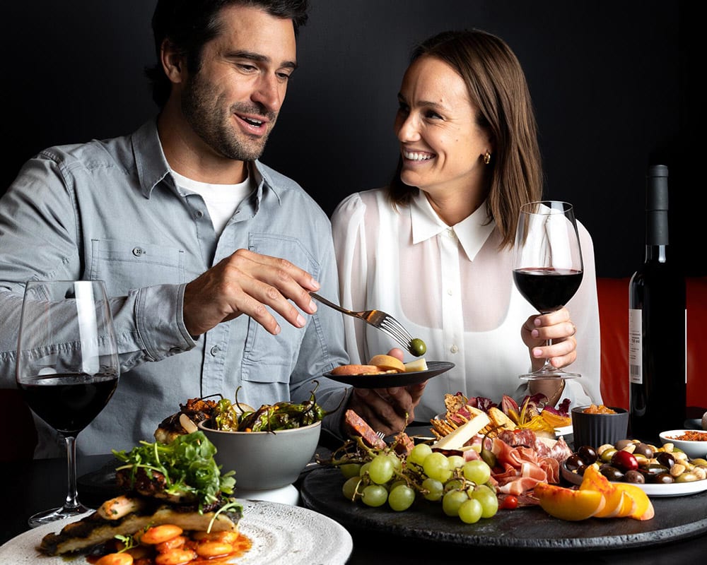 A couple enjoying wine and charcuterie while attending Cornucopia Whistler, a food and drink festival.