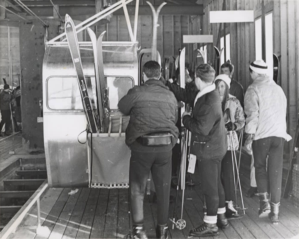 Vintage black-and-white photograph of skiers loading skis into a gondola cabin at a Whistler ski resort lift station.