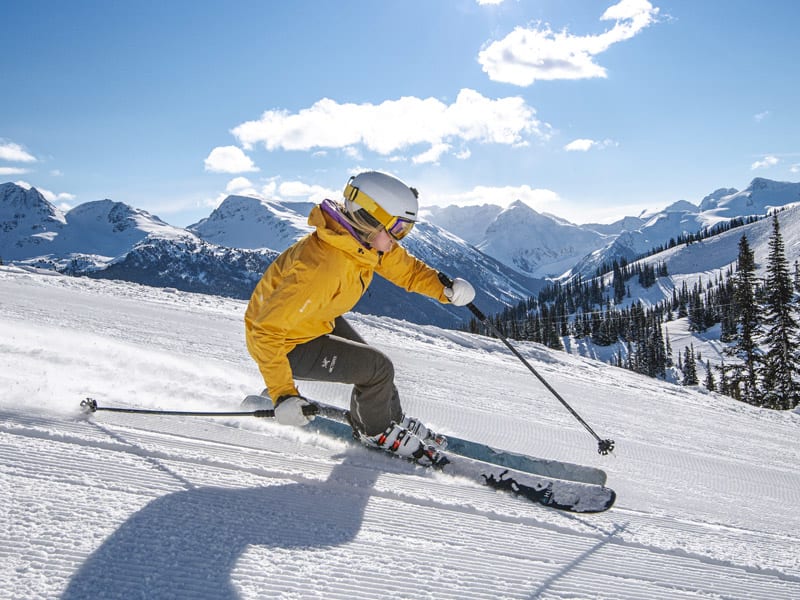 Skier in yellow jacket carves down a groomed run on Whistler Blackcomb.
