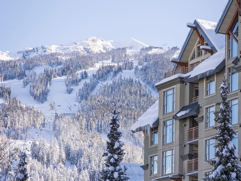 Snow-covered Whistler Village accommodation with ski runs and forested slopes rising across Whistler Mountain in winter.