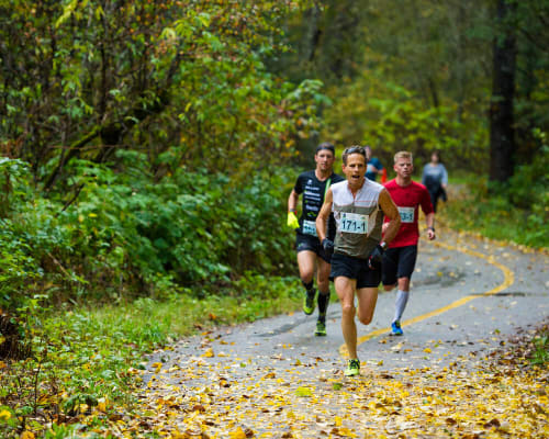 Runner wearing bib number 171-1 leading a pack along a leaf-covered forest trail in autumn in Whistler, BC.