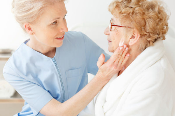 Freundliche Pflegerin cremt Seniorin im Gesicht ein