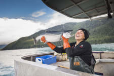 fisherwoman holding salmon on back deck of a boat