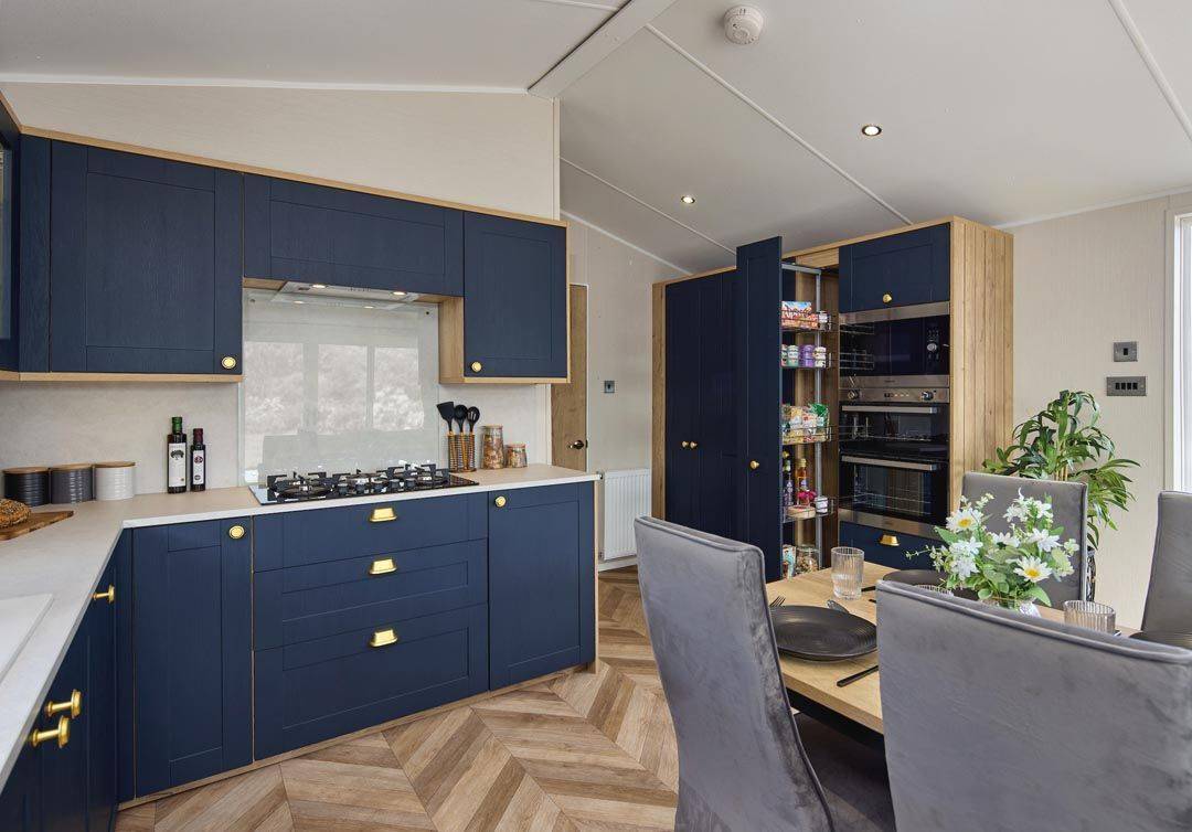 The Willerby Gainsborough luxurious kitchen is equipped with blue cabinet doors and gold accents, topped with a white marble effect worktop.