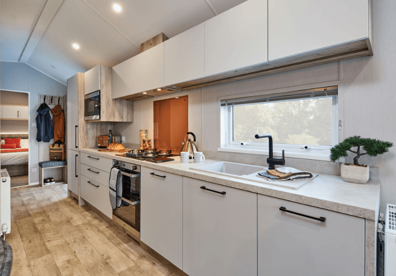 The Willerby Astoria stylish linear kitchen with white cupboard doors and an orange splashback.