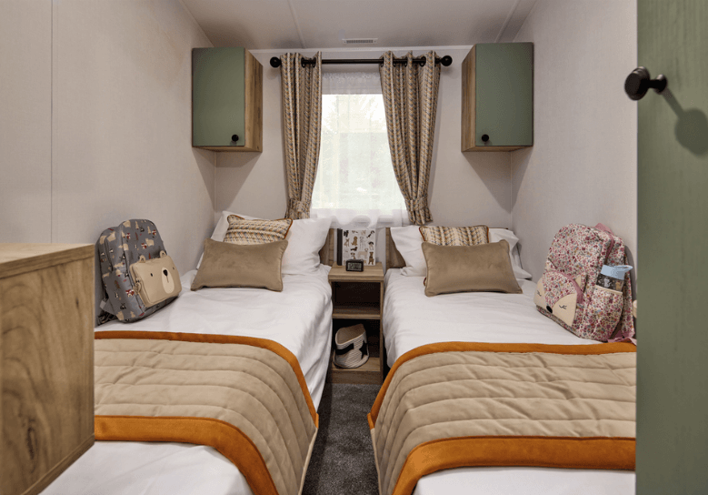 A twin bedroom in the Willerby Buxton holiday home. Two single beds have red throws to contrast with the green and cream colour scheme. A large window lets in plenty of light. 