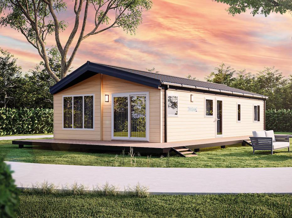 The Willerby Clearwater exterior is in a creamy yellow with a brown decking surrounding it. The Lodge is placed on a grassy field surrounded by bushes.