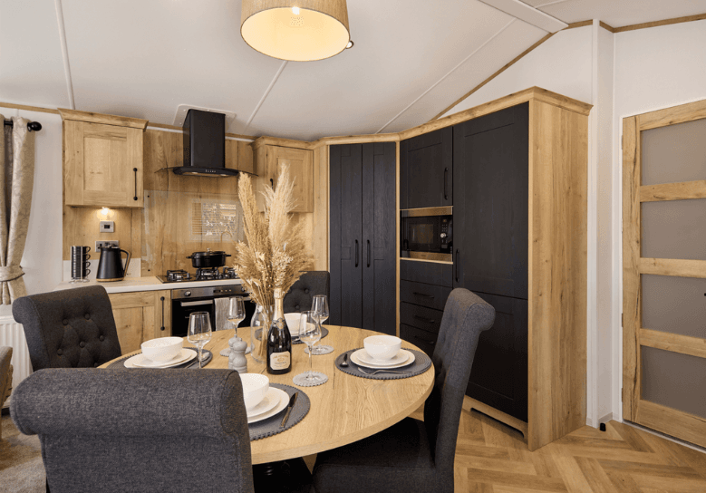 The Willerby Dorchester open-plan kitchen with an attractive round dining table that is adorned with fabric black chairs matching the rest of the kitchen.