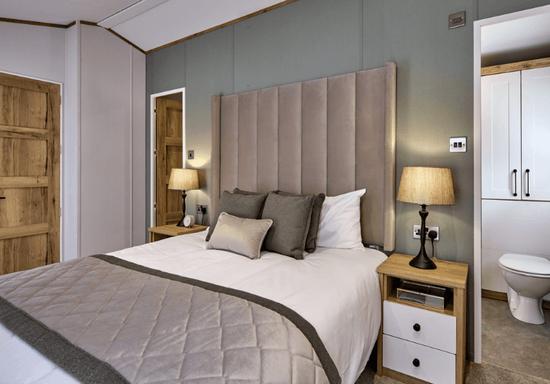 The Willerby Dorchester stylish master bedroom with a grey upholstered headboard featuring a walk-in wardrobe and an ensuite bathroom.