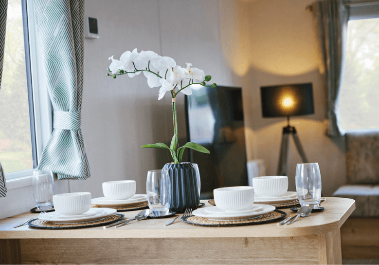 The Willerby Ellerton Extra dining table has an oak effect dining table and chairs, with white crockery and a centerpiece. 