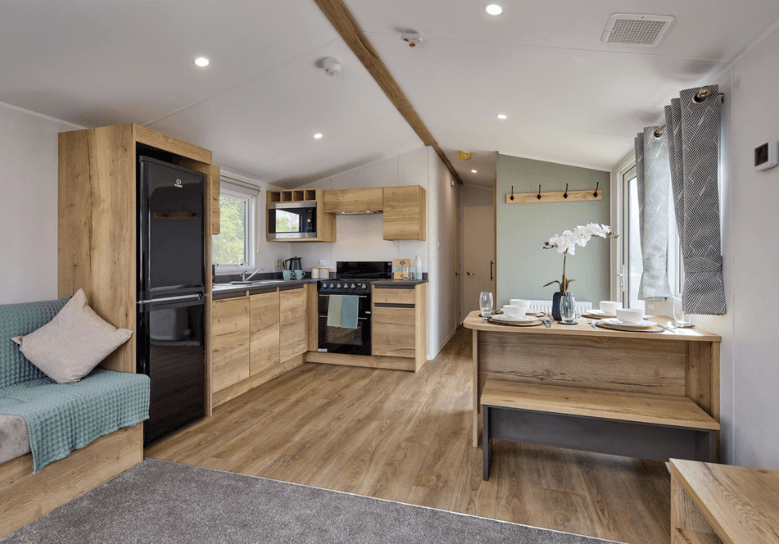 The Willerby Ellerton Extra open-plan kitchen and dining area has oak effect storage units adorned with black appliances.
