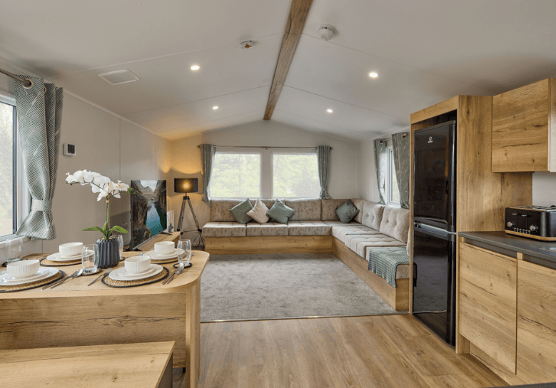 The Willerby Ellerton Extra lounge with fixed grey seating with soft green furnishings, and an overview of the oak effect units in the kitchen and dining area.