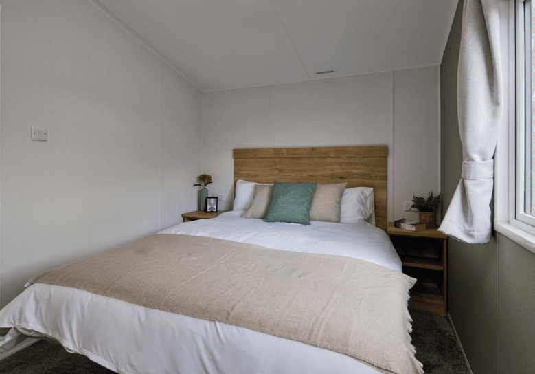 The Willerby Ellerton Extra modern master bedroom has a soft green accent wall with cream and green furnishings to match the colour scheme of the home.