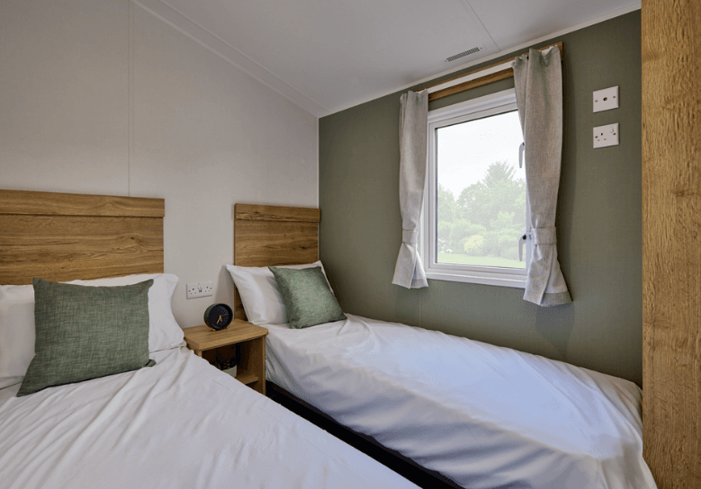 The Willerby Ellerton Extra twin bedroom has oak effect storage units and a green accent wall with matching soft furnishings.