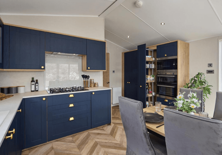 The Willerby Gainsborough luxurious kitchen is equipped with blue cabinet doors and gold accents, topped with a white marble effect worktop.