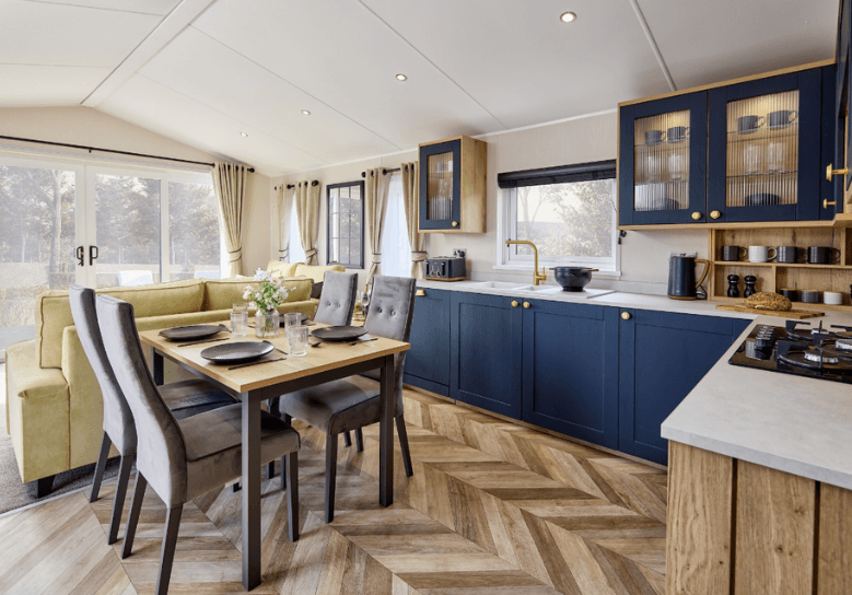The Willerby Gainsborough luxurious kitchen is equipped with blue cabinet doors and gold accents, topped with a white marble effect worktop.