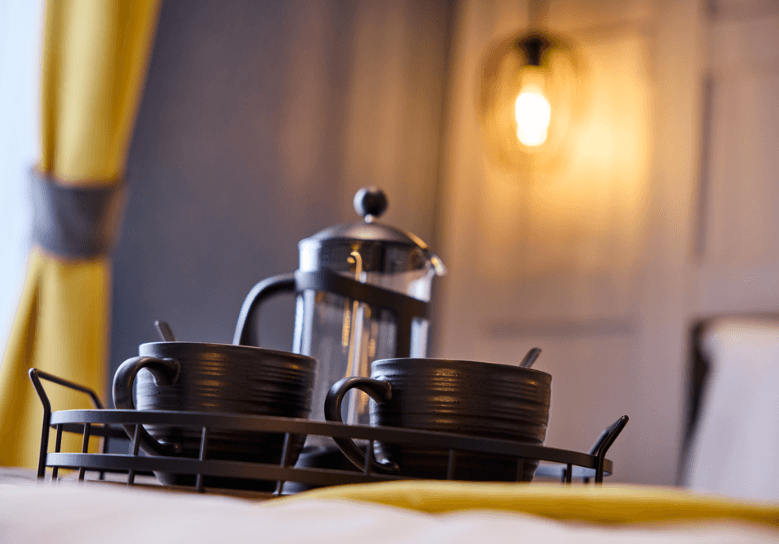 Cafetiere and two black mugs on a black tray on the master bed.