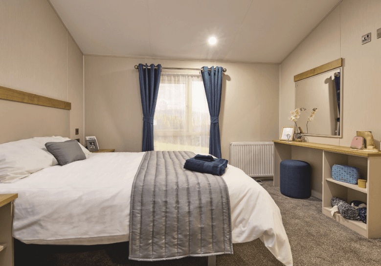 The Willerby Hayward master bedroom has a oak effect dressing area with storage and blue soft furnishings.
